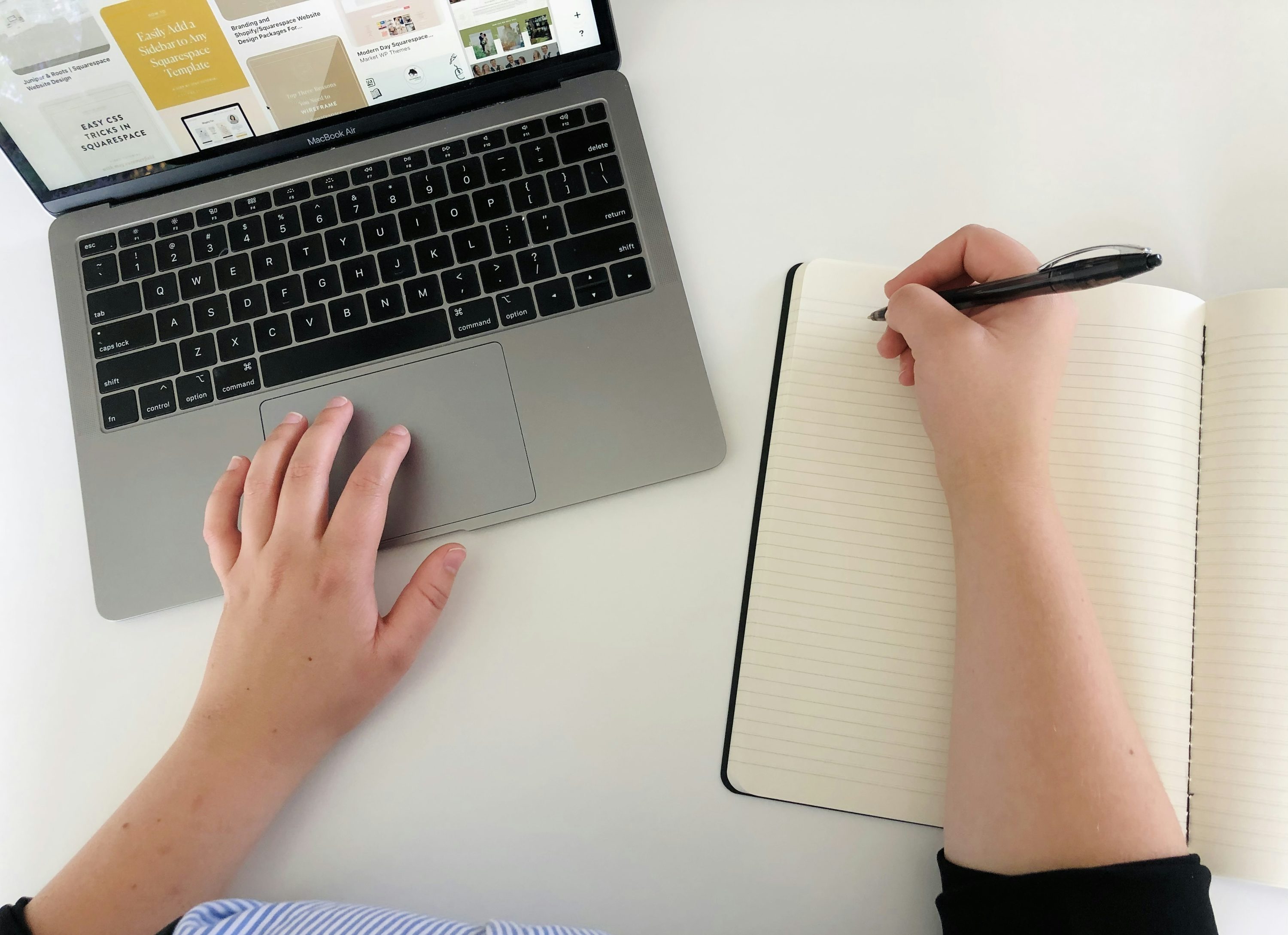A person researches at a laptop and writes notes in a notebook